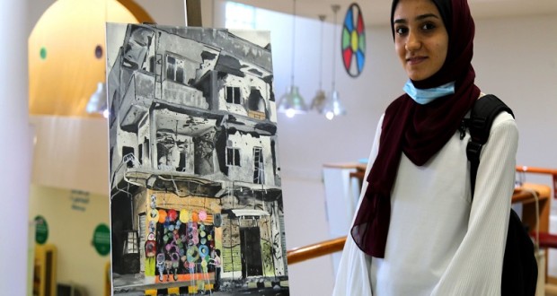 وعد البياري (16 عاماً) تقف بجانب رسمة رسمتها ضمن مشاركتها في نادي الرسام الصغير