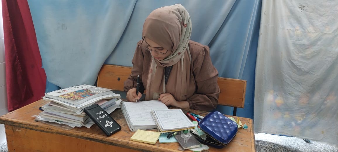 على مقعد بجانب خيمة نزوح عائلتها تواصل مي دراستها
